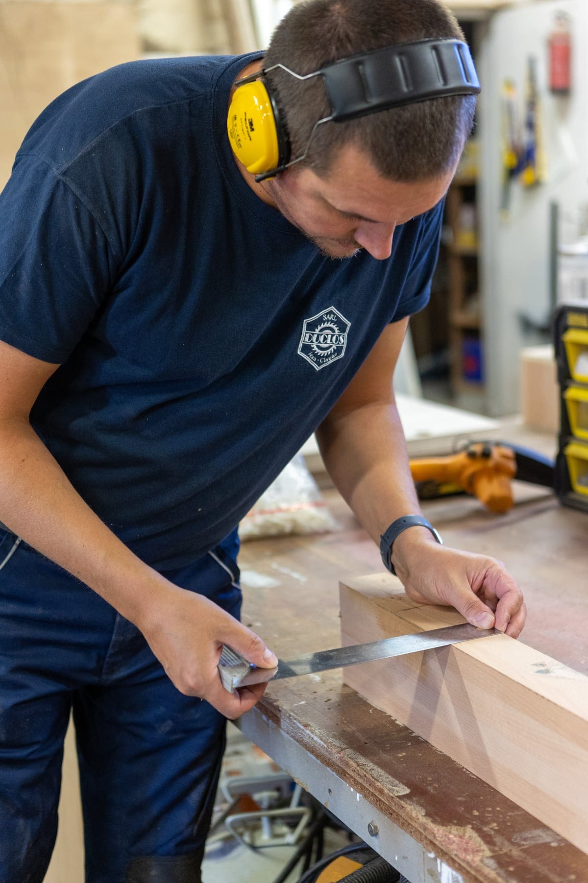 Un menuisier mesure et trace une pièce de bois à l’atelier